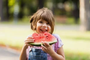 niña comiendo sandía en un parque. comidas de verano para niños, refrescantes y saludables