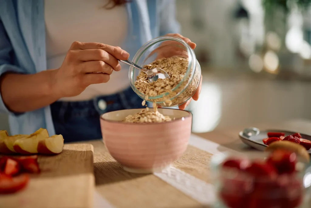Persona sirviendo copos de avena en un bol junto a frutas frescas, opción rica en fibra soluble para regular la glucosa