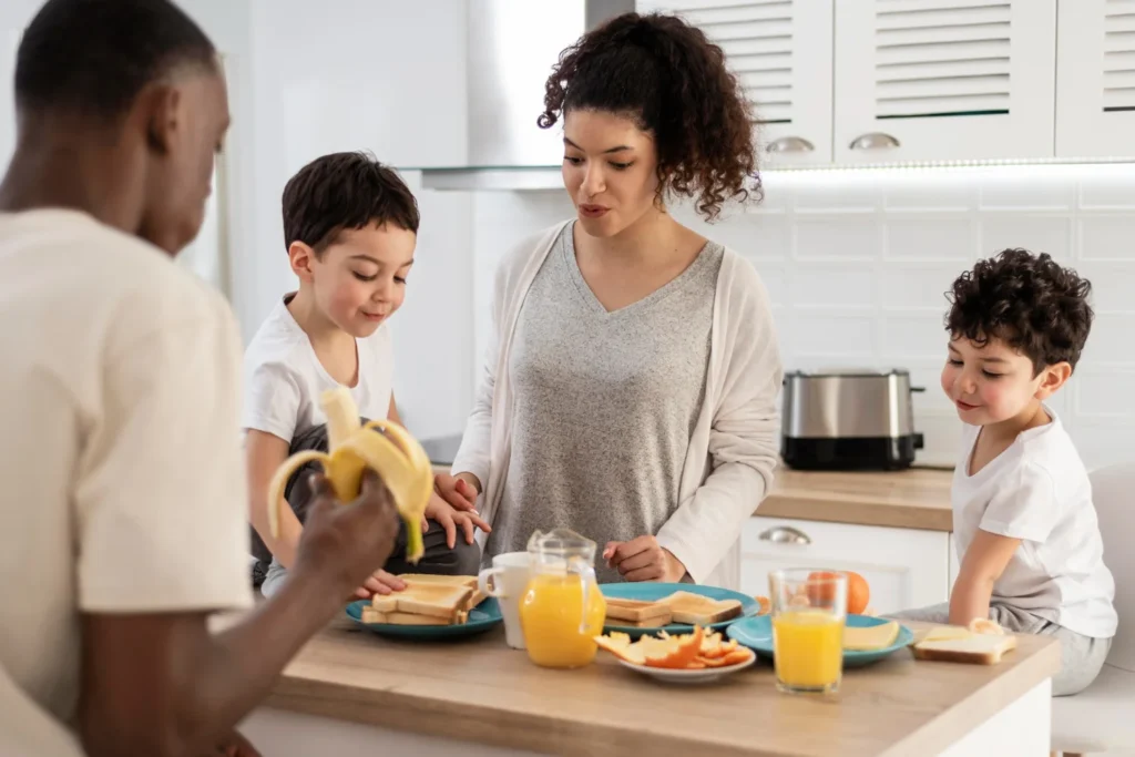 Familia con niños preparando un desayuno saludable con frutas en la cocina con asesoramiento en nutrición infantil.