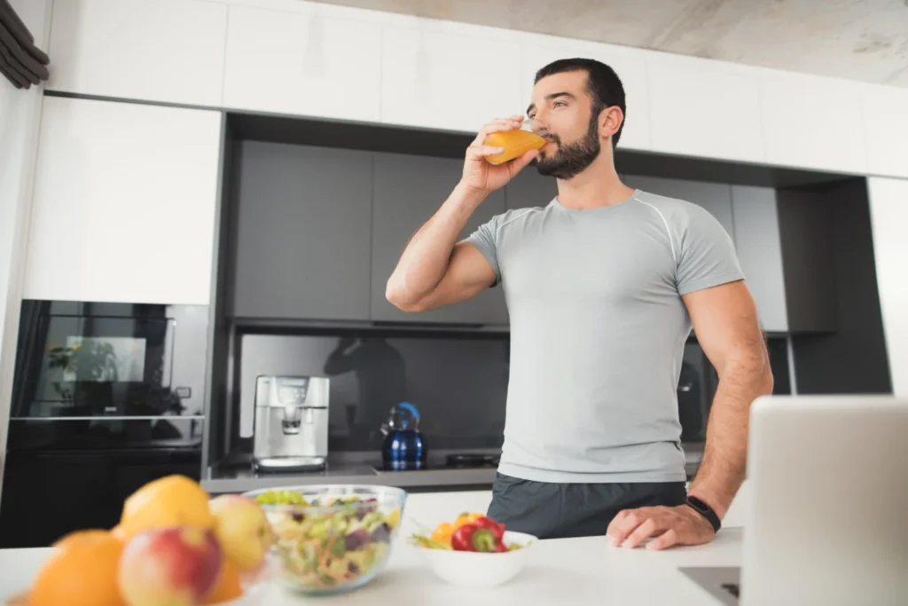 Hombre deportista bebiendo un batido de proteínas saludable en la cocina tras su plan de nutrición deportiva