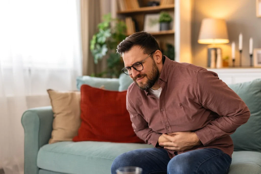 Hombre sentado en el sofá sujetándose el abdomen con dolor por problemas de SIBO y molestias digestivas.